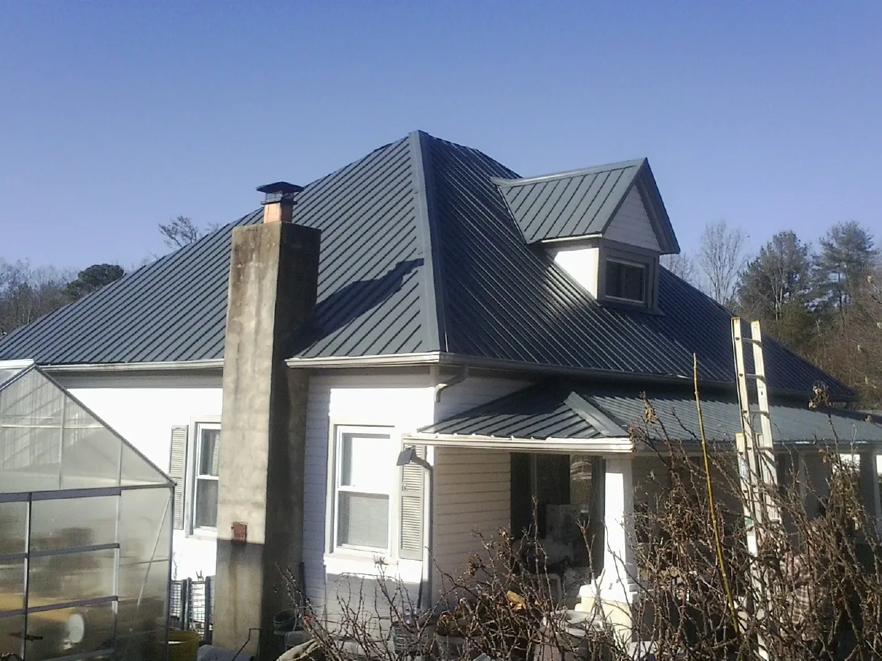 Dark blue standing seam metal roof on a white farmhouse with dormer — Slate & Tile Roof Repair by Roofing Brothers in Newtonsville
