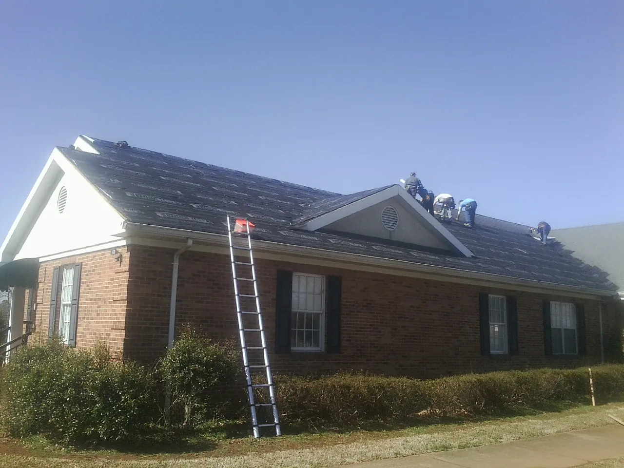 Crew tearing shingles off a brick ranch roof with a ladder set — Metal Roof Repair work by our crew in Newtonsville