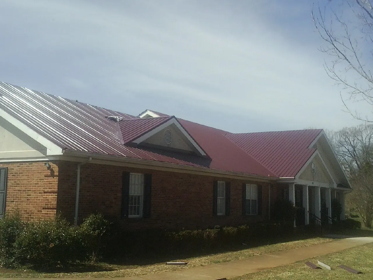 Red metal roof with gabled entries on a long brick building, from a Hail Damage Roof Repair job in Newtonsville