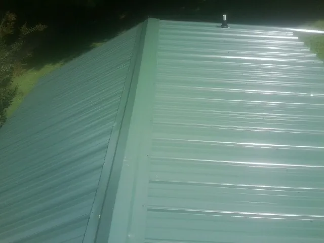 New green metal panels meeting at the ridge of a roof — Flat Roof Repair work by our crew in Newtonsville