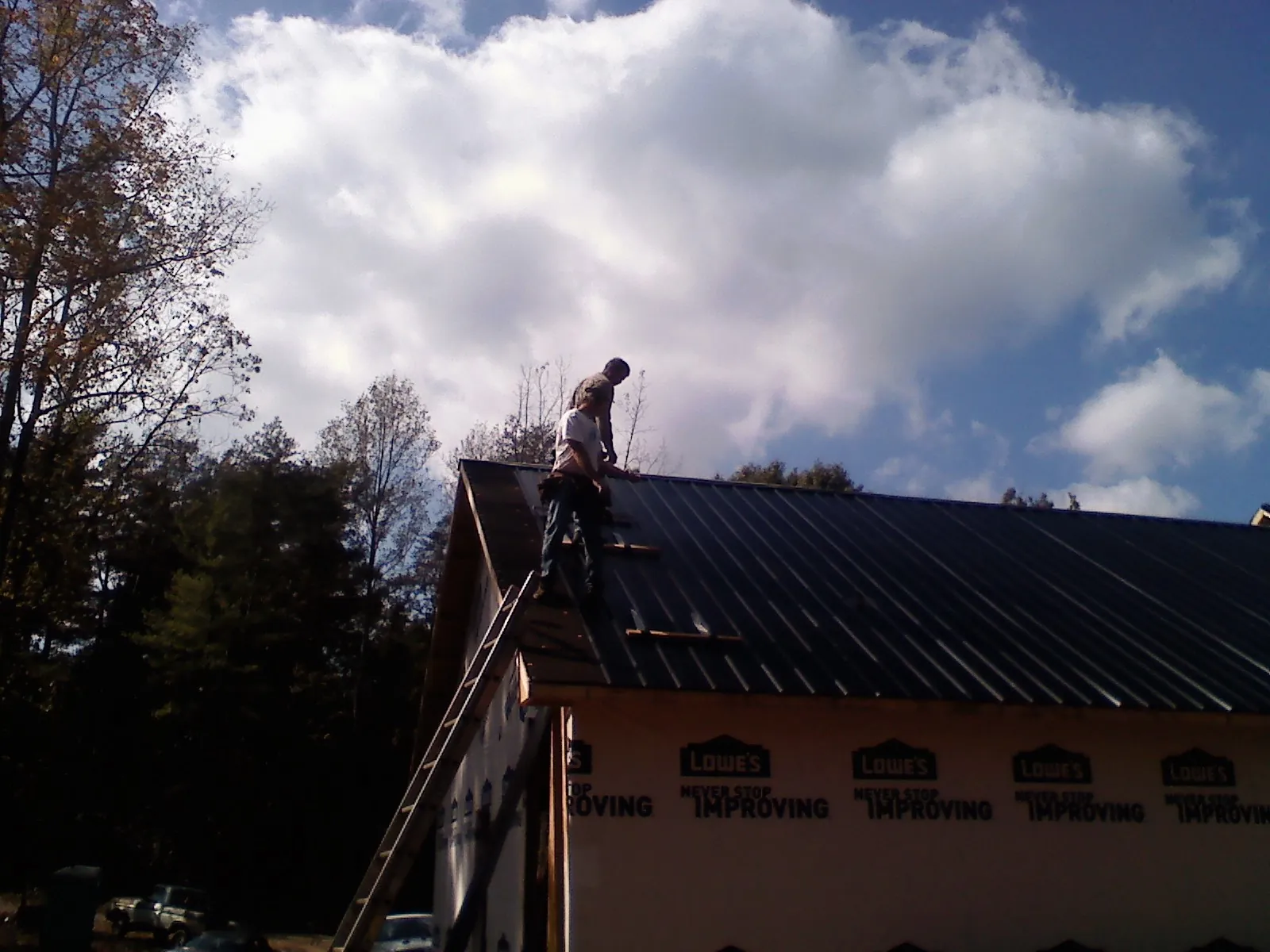 Roofer fastening dark metal panels high against a cloudy sky, from a Roof Inspection job in Newtonsville