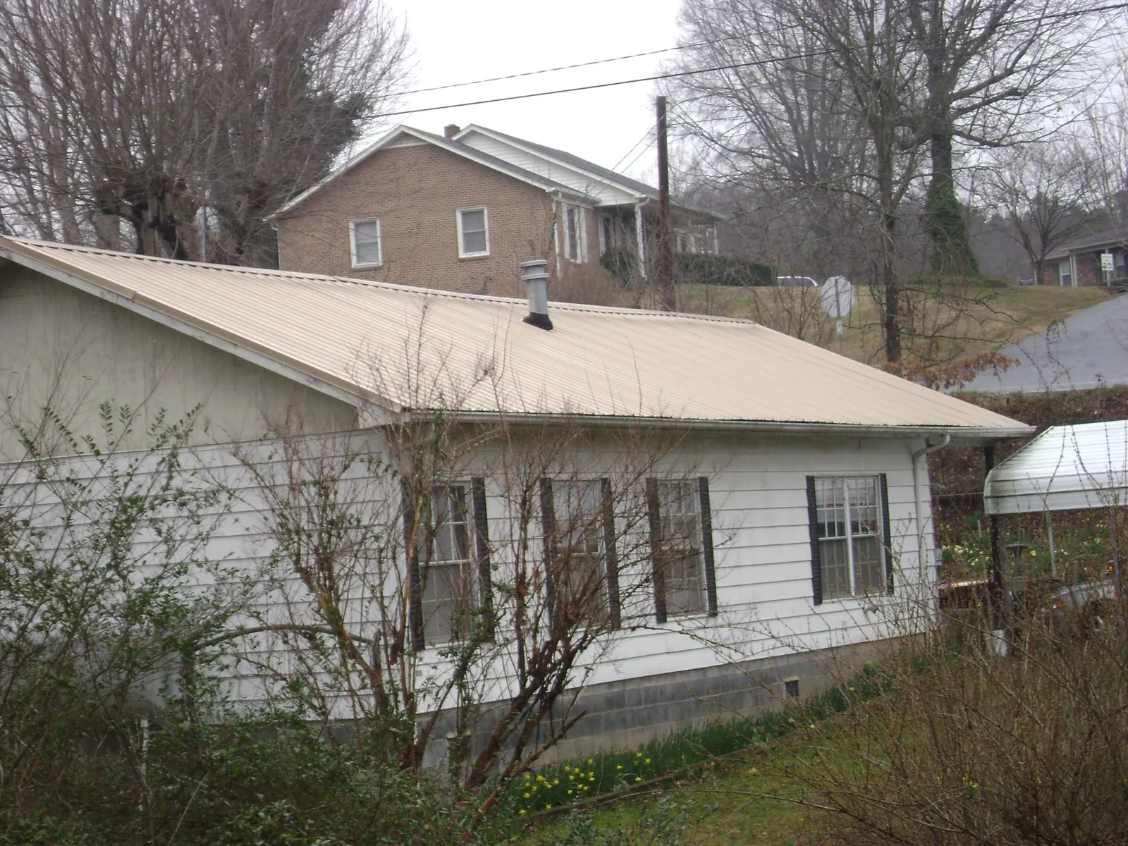 Tan metal roof on a white sided house set into a hillside — Commercial Roofing by Roofing Brothers in Newtonsville