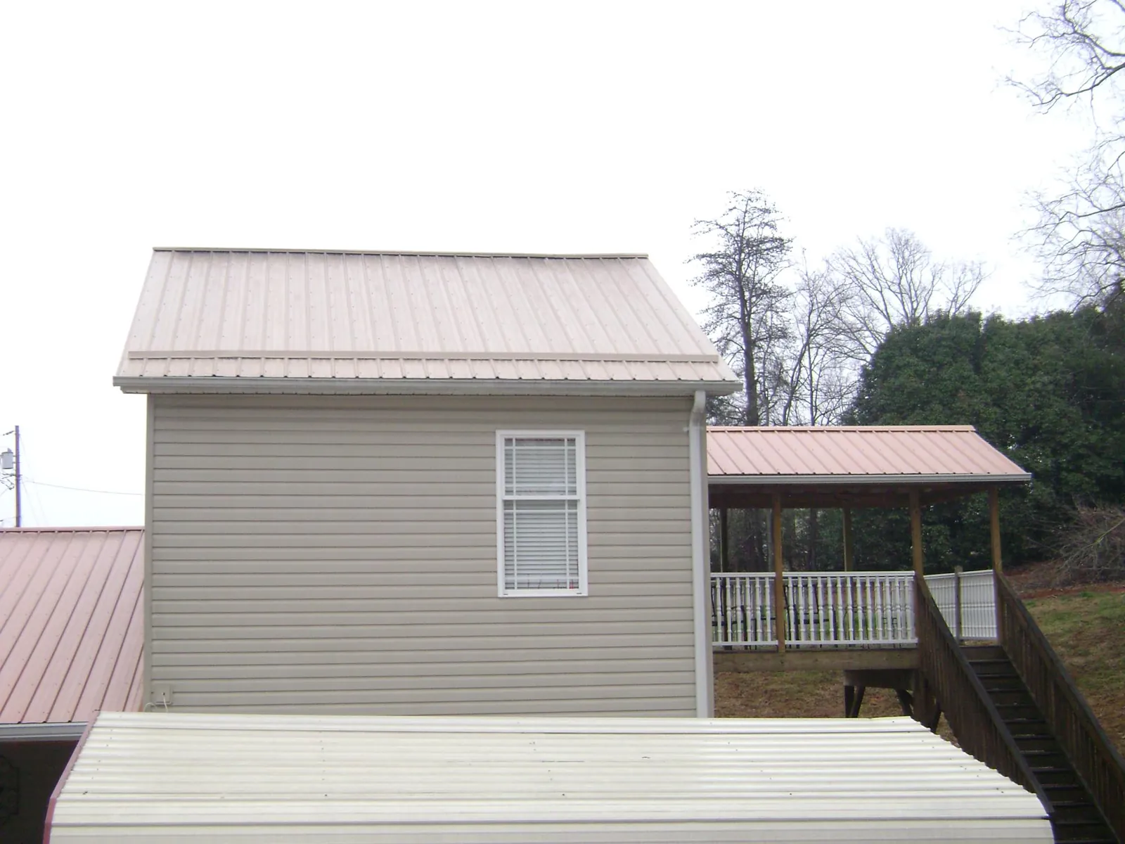 Tan metal roofs on a two story addition and attached porch, from a Roof Replacement job in Newtonsville